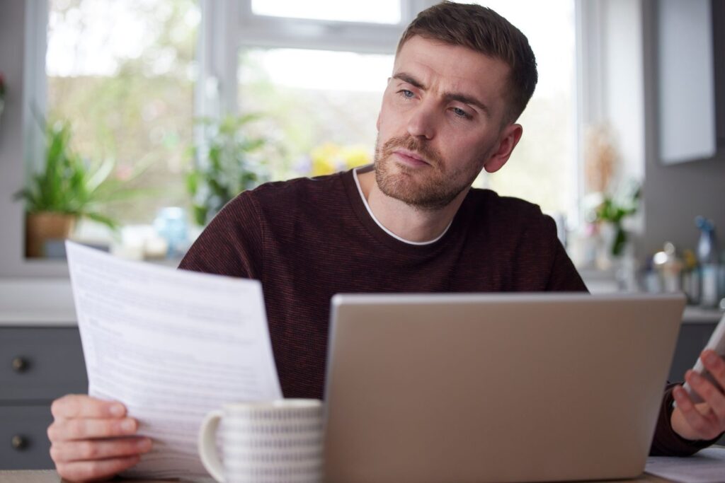 Un homme consultant une facture devant son ordinateur portable